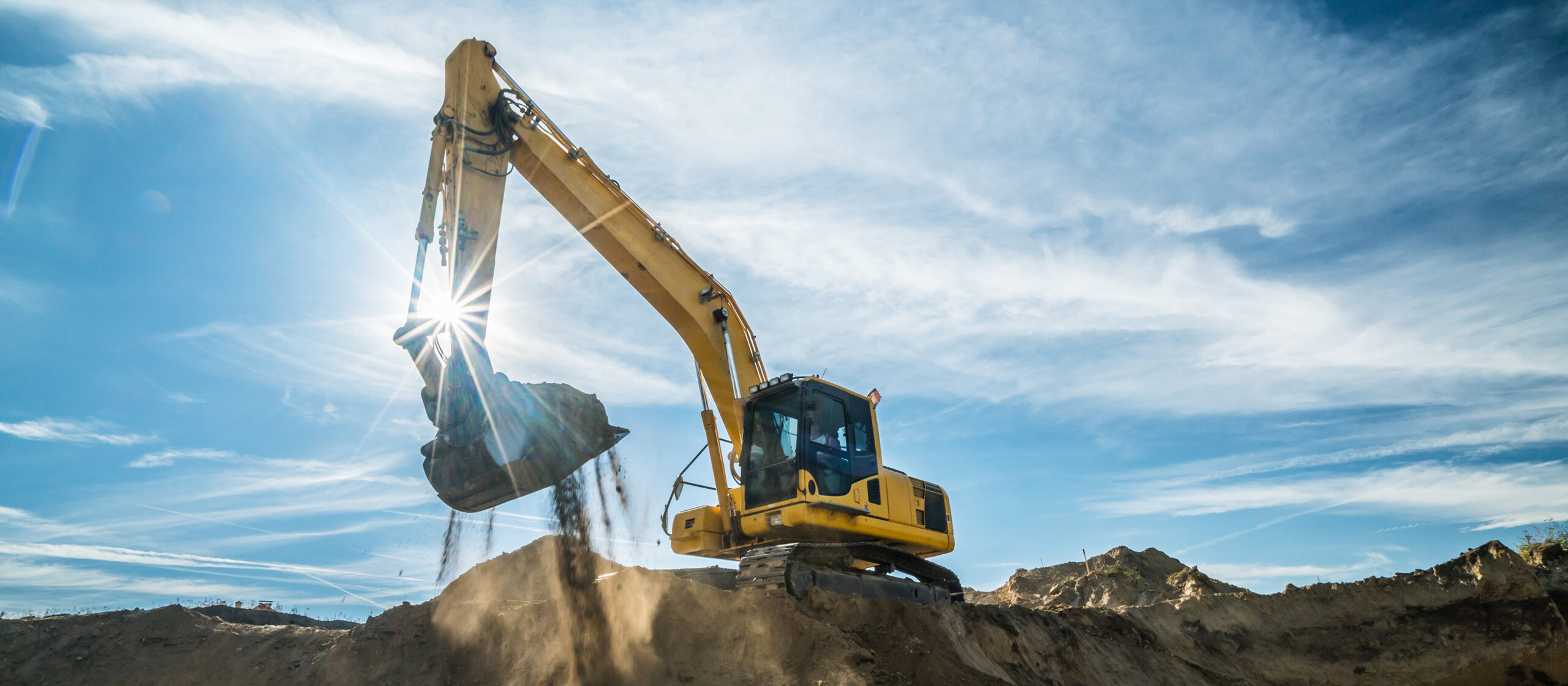 Excavator scooping dirt against a bright sky, using Shell PANOLIN biodegradable hydraulic fluid